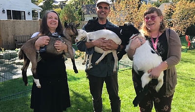 three library staff holding baby goats banner