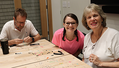 two patrons smile at the camera next to their jewelry projects banner